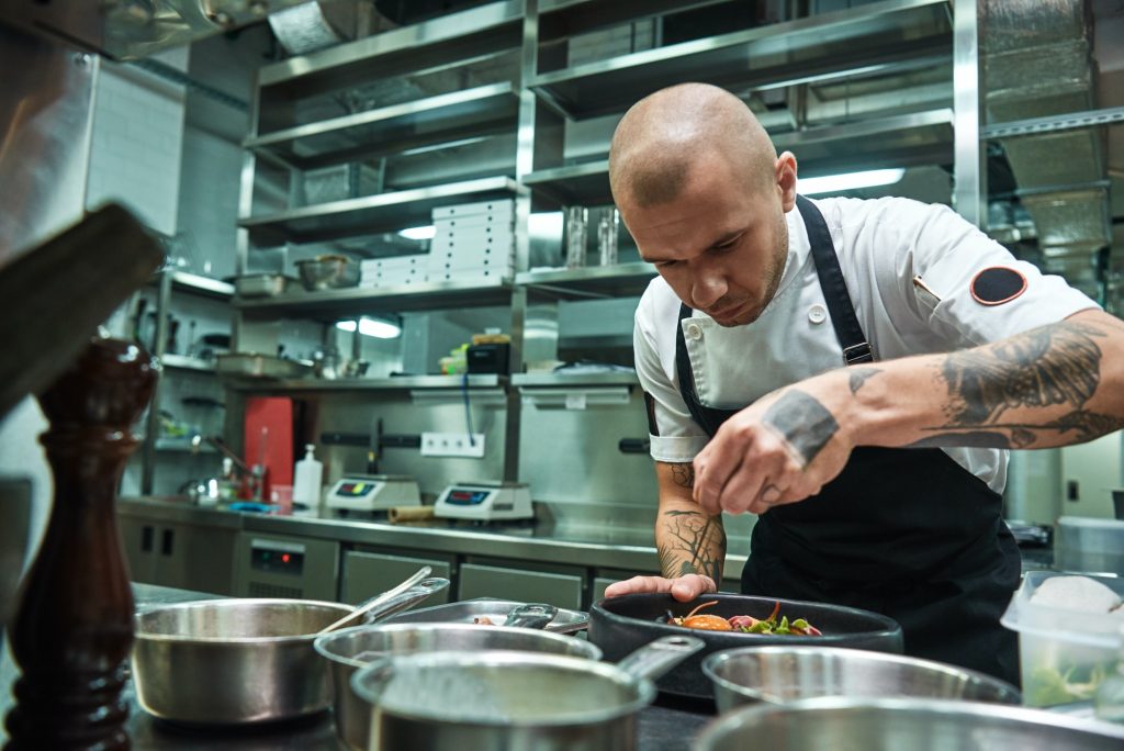 Delicate work. Famous confident chef with several tattoos on his arms garnishing pasta Carbonara in